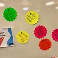 Photo of some brightly coloured gear-wheel shaped cards with feedback written on, affixed to a whiteboard