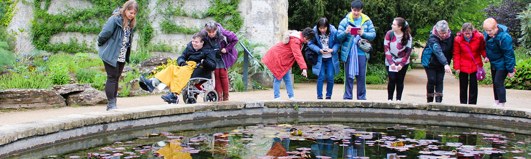 People enjoying a workshop at the Oxford Botanic Garden looking into a pond together