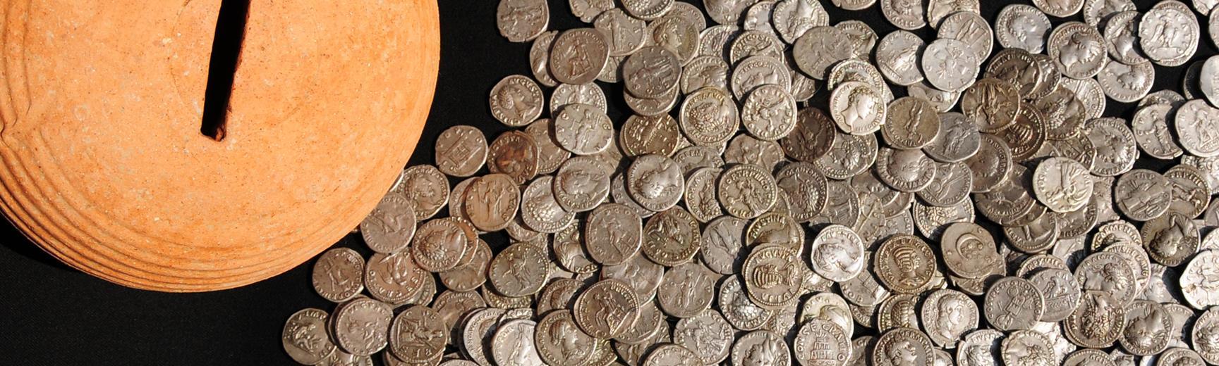 Old silver coins next to a terracotta pot