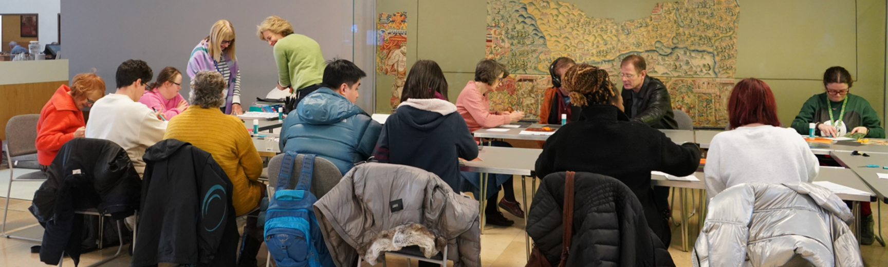 A group of adults around a large group of tables forming a circle doing crafts together.