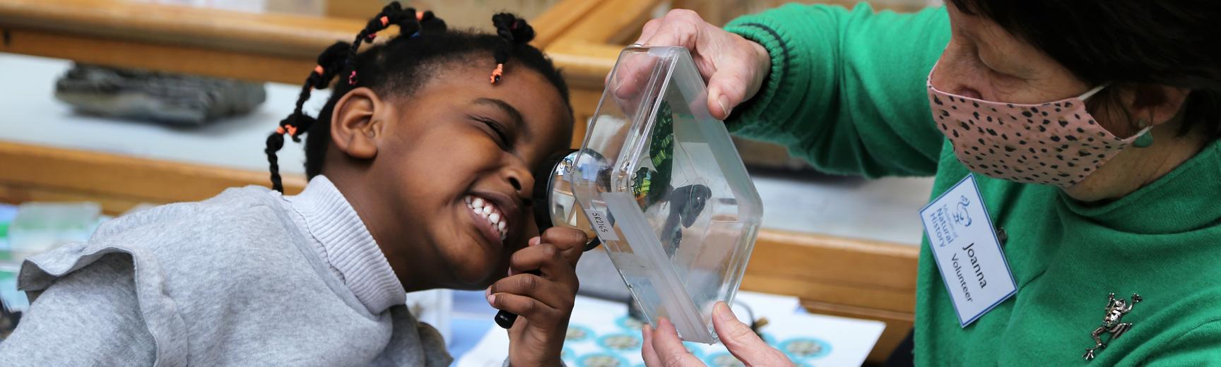 A young girl looks at an insect with a magnifying glass