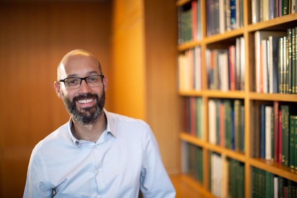 Man smiling stood beside bookcase