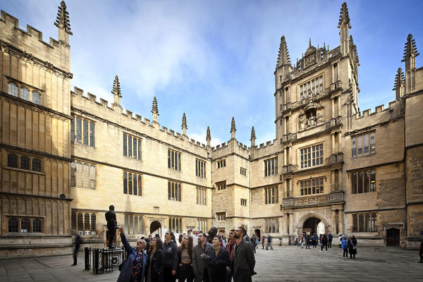 A group of individuals stand together in the stone quadrangle of the Bodleian Old Library