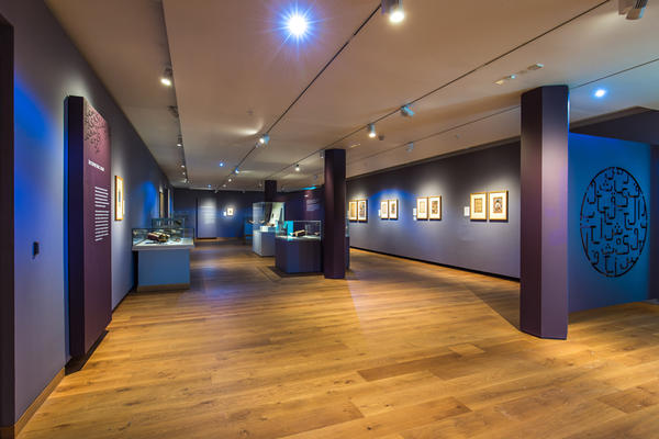 Museum exhibition with framed prints on walls and objects in cases