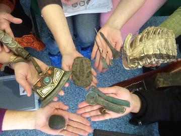 Picture1 hands in a circle holding museum objects: a small dinosaur footprint cast, a Tibetan striker, a Scarab charm, an Elephant tooth and some metal pins and keys