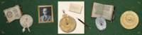 a collection of antique astrolabes, sundials, books, a black and white photograph of Lewis Evans, and a note card and pen, on a green surface