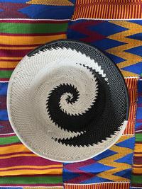 a black and white spiralled woven bowl sitting on a multicoloured woven mat with lines and zig zags