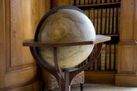 Image shows an antique standing Globe in front of a bookcase, with dark wood finishing to its supports.
