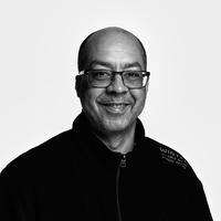 Black and white photograph of a man wearing glasses and a zip-up jumper.