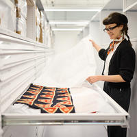 A woman removes tissue paper from a metal storage drawer, revealing an item of textiles.