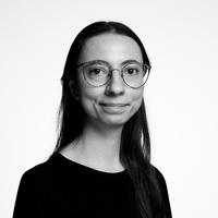 Black and white headshot of a brunette lady, who wears round glasses and a black top.