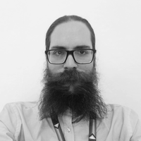 Black and white photograph of a male member of staff, who has a beard and wears rectangular glasses.